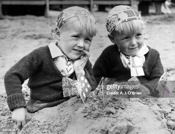 Twin brothers on the beach at Weston-super-Mare with flags in their sandcastle.
