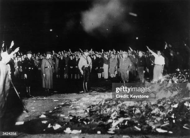 German soldiers and civilians give the Nazi salute as thousands of books smoulder during one of the mass book-burnings implemented throughout the...