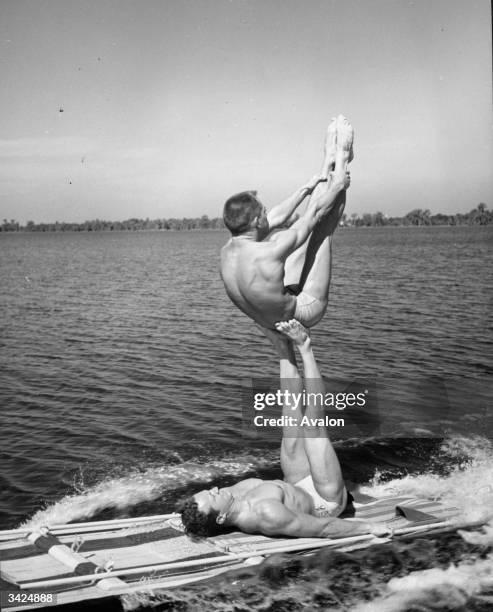 Two athletes practising a gymnastic 'aqua acrobatic' exercise on a water toboggan at Cypress Gardens, Florida.