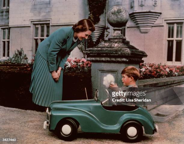 Princess Elizabeth watching her son Prince Charles playing in his toy car while at Balmoral.