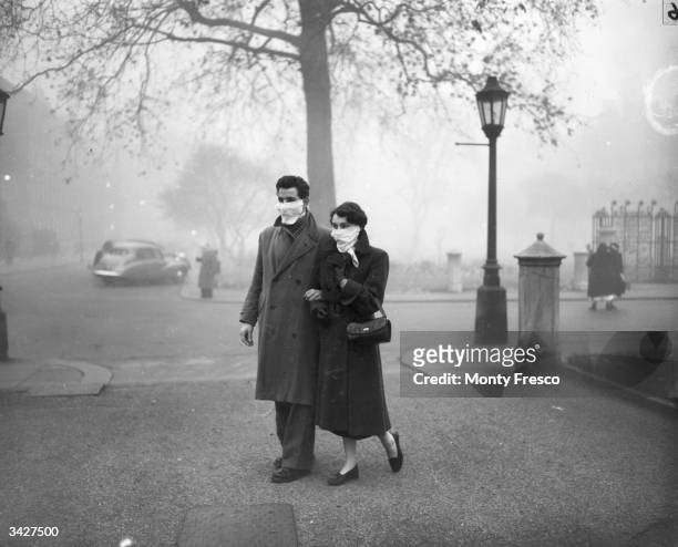 Couple walking in London wearing smog masks on a foggy day.