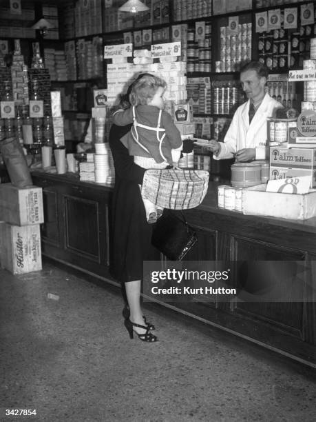 In the first week of rationing in WW II a housewife hands over her ration books to a grocer before buying food.