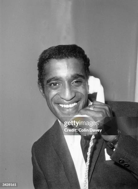 American actor, singer and dancer Sammy Davis Jnr phones his wife upon his arrival at London Airport.