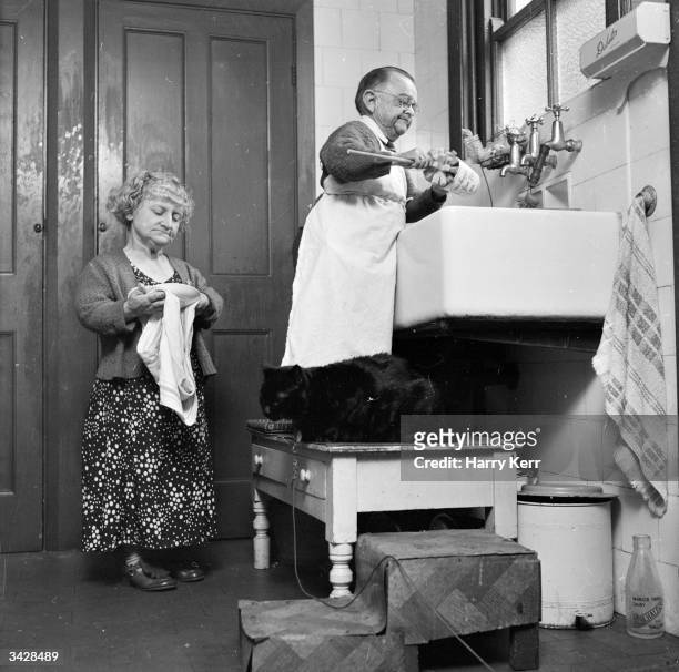 Henry Behrens, the smallest man in the world stands on a table to do the washing up in the kitchen of his Worthing home. Measuring only 30 inches...