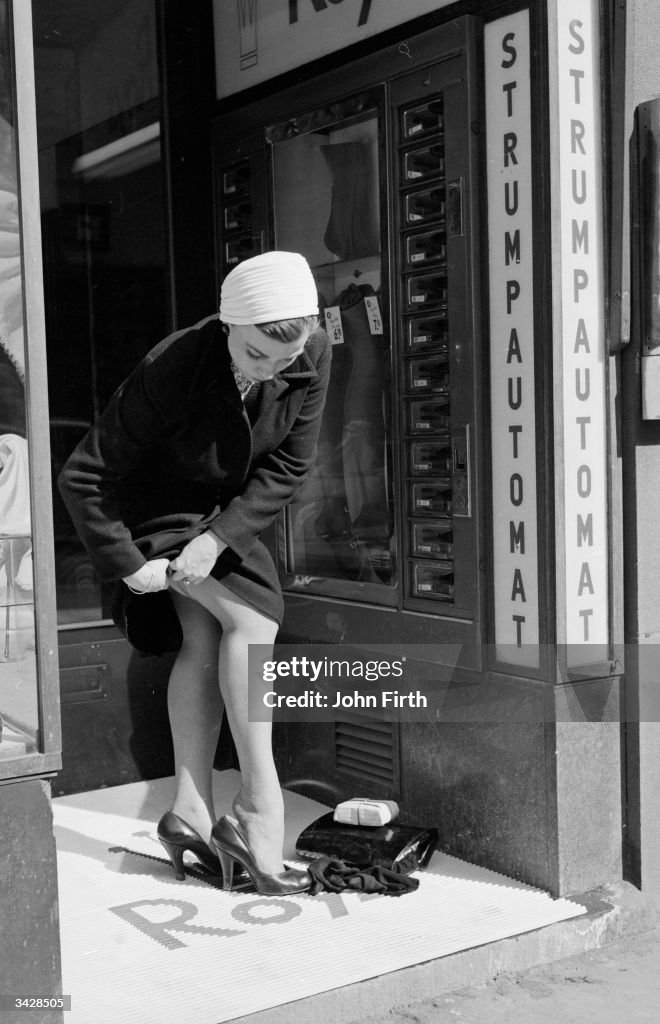 A Woman Buys A New Pair Of Nylons From A Stocking Vending Machine Or a-woman-buys-a-new-pair-of-nylons-from-a-stocking-vending-machine-or