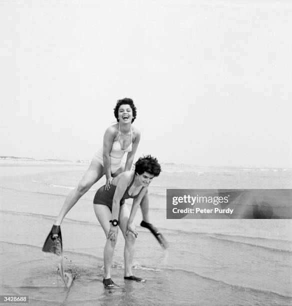 Two women wearing fins play leap-frog on the beach.