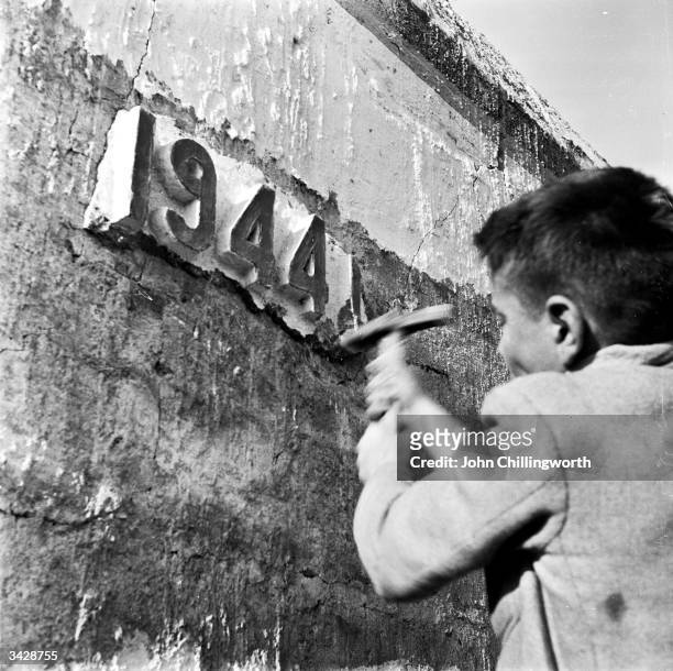 Young boy chips off part of the plaster date '1944' on the last remnant of Hitler's Atlantic Wall in Courseulles-sur-Mer, the first French port to be...
