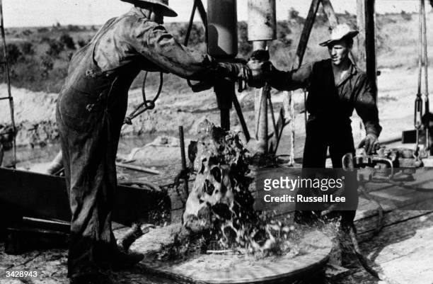 Two workmen adding a length of drilling pipe at an oil well in the Seminole Oil Field, Oklahoma.