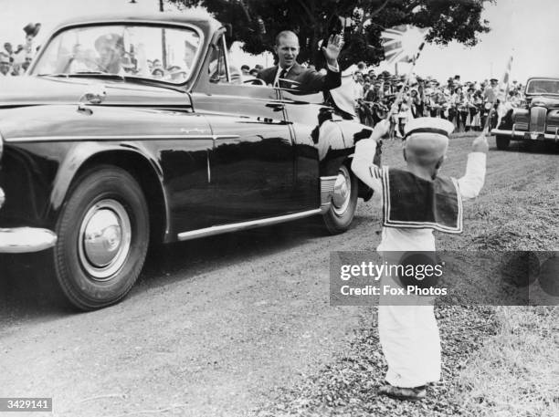 Seated beside Queen Elizabeth II, the Duke of Edinburgh waves to an enthusiastic little sailor, four-year-old Michael McCarthy during a tour of...