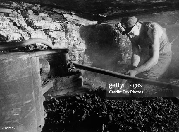 Crouched in a cramped shaft, a coal miner hacks at the coalface at Ashington Colliery in Northumberland.