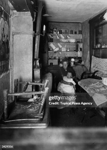 An old woman nursing a baby in the scullery of a run-down house in Crosland Square, Bethnal Green, London.