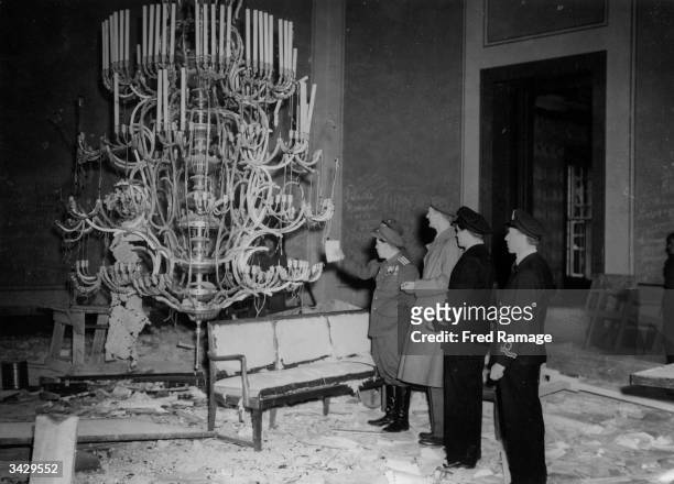 Conquering allied officers examine a chandelier amidst the bomb damaged grandeur of what was the Banqueting hall in Hitler's Chancellory following...