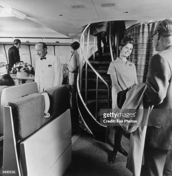 Air hostess greets a passenger in front of a spiral staircase which leads to the upper deck lounge in a Boeing 747 Monarch, wide-cabin jet aircraft.