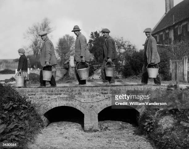 Villagers of Imber in Wiltshire returning home with water drawn from one of the village's only remaining wells. The spring over which they are...