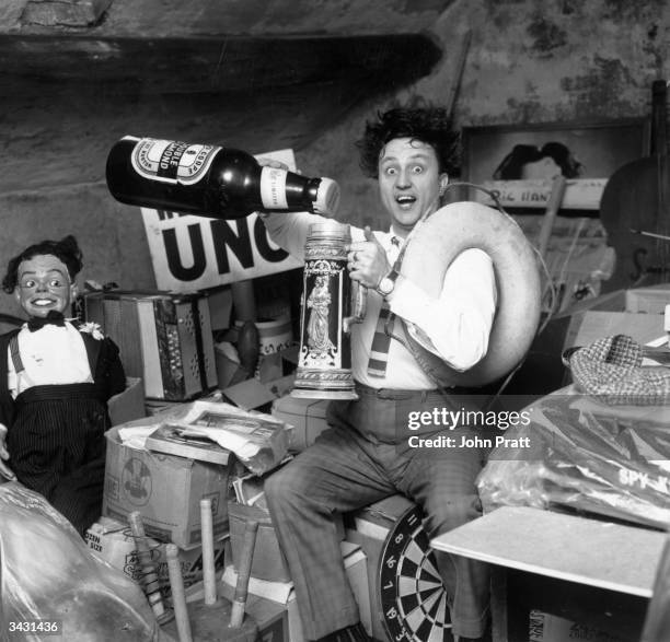 Liverpudlian comedian Ken Dodd sorts through a heap of junk, including a ventriloquist's dummy, an old tankard and a giant beer bottle in the attic...