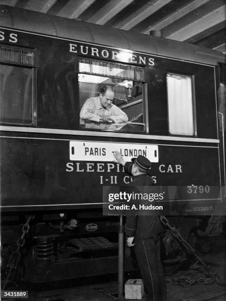 Passenger in pyjamas leans through a window on Southern Railway's Dover-Dunkirk cross-channel train ferry service to chat to an attendant prior to...