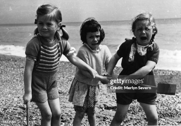 Young girls argue and fight over whos turn it is to dig to Australia, on their first visit to the sea. Original Publication: Picture Post - 4191 -...