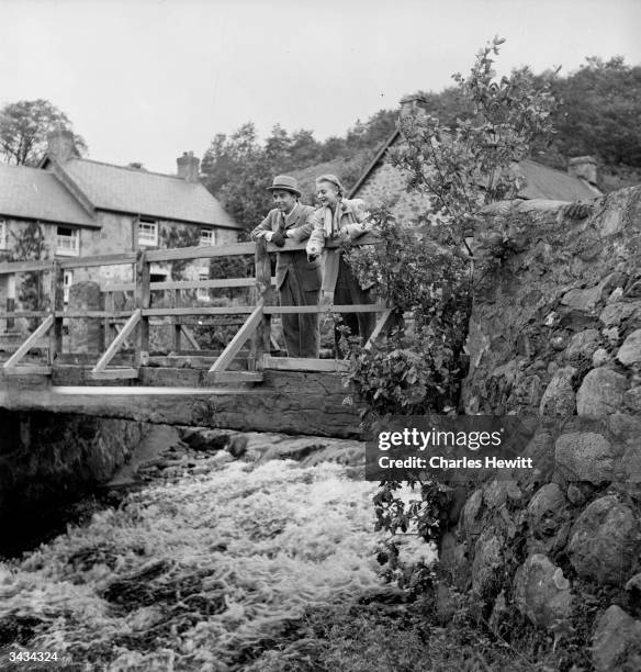 Welsh film actor and director Emlyn Williams and his co-star Andrea Lea admire the view from the bridge in Rhydymain, Merioneth, where they are...