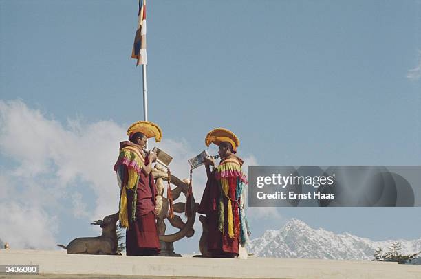 Two Gelugpa monks in ceremonial robes blow conch shells on the roof of the Dalai Lama's temple in Dharamsala to announce the arrival of His Holiness...