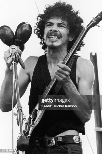 Mexican-born American guitarist and bandleader Carlos Santana holds maracas and an electric guitar while performing at the Woodstock Music Festival...