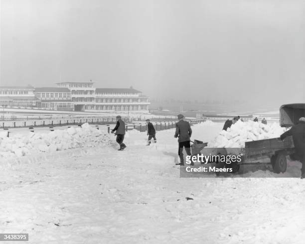 Teams of men clear the snow from Cheltenham racecourse before the venue reopens on March 12th. The work has to be done by hand, since machines would...
