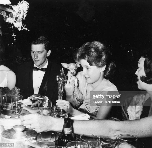 American actor Patty Duke holds her Oscar statuette and her pet chihuahua, Bambi, while seated next to Andy Prine during the Academy Awards party...