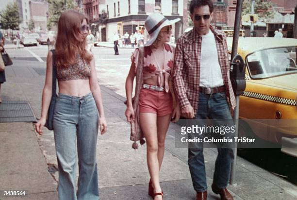 American actors Jodie Foster, center, and Robert De Niro walk past a parked taxi on a New York City street in a still from the film, 'Taxi Driver'...