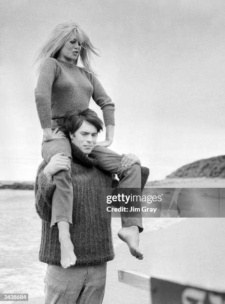 French actor Laurent Terzieff giving Brigitte Bardot a piggy-back ride on the beach at North Berwick, Scotland, in a scene from the film 'Two Weeks...