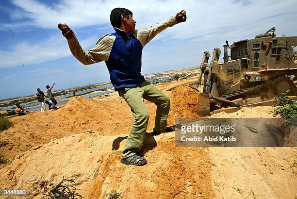 Palestinians throw rocks towards an army bulldozer during clashes with Israeli soldiers April 20, 2004 near the Beit Lahyea Refugee Camp, in the Gaza...