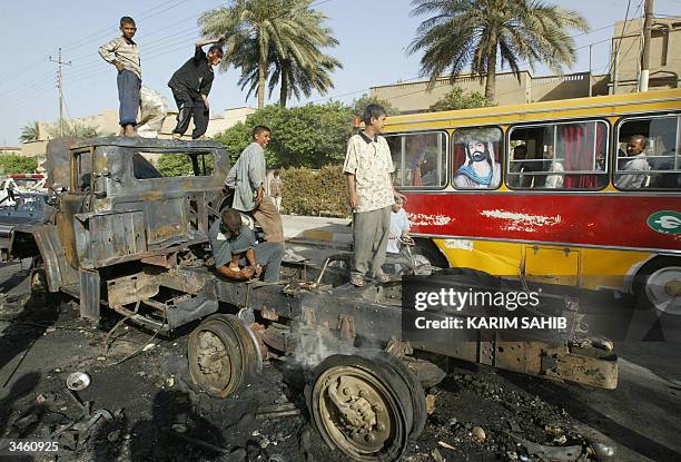 Bus decorated with a portrait of Shiite Imam Ali drives past Iraqi children looting a burnt Bulgarian military truck 23 April 2004 in Karbala. A...