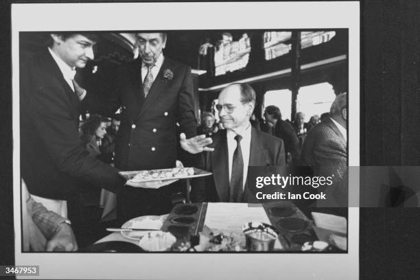 Eat Yourself Slim weight-loss guru Michel Montignac looking over a tray of hors d'oeuvres which waiter is holding out for his inspection as he sits...