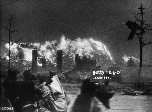 People hurry past a fire burning in the wake of an air raid, Japan, circa 1945.