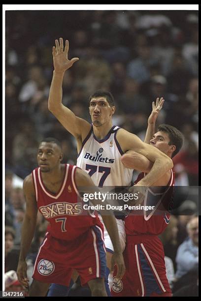 Center Gheorghe Muresan of the Washington Bullets and Philadelphia 76ers player Mark Bradtke look for the ball during a game at the USAir Arena in...