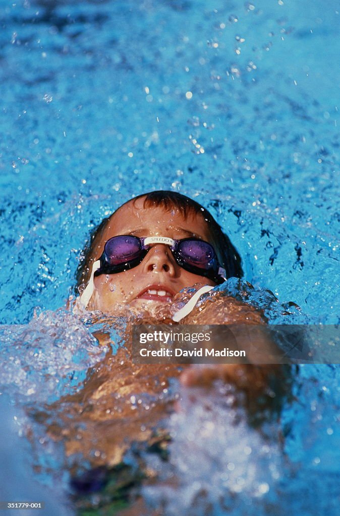 Boy (6-8) in goggles doing backstroke in swimming pool