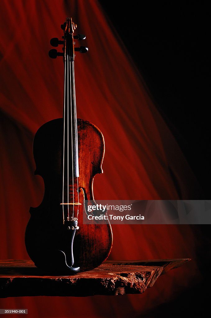 Violin on rough wooden shelf,dark red streaked background