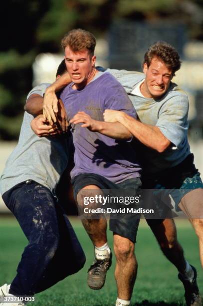 three men playing recreational football in park - tackling stock pictures, royalty-free photos & images