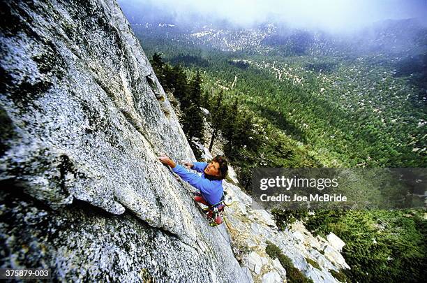 female climber scaling steep, granite rock face, elevated view - soloklettern stock-fotos und bilder