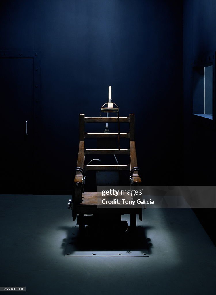 Electric chair in dark empty room,  light streaming from above