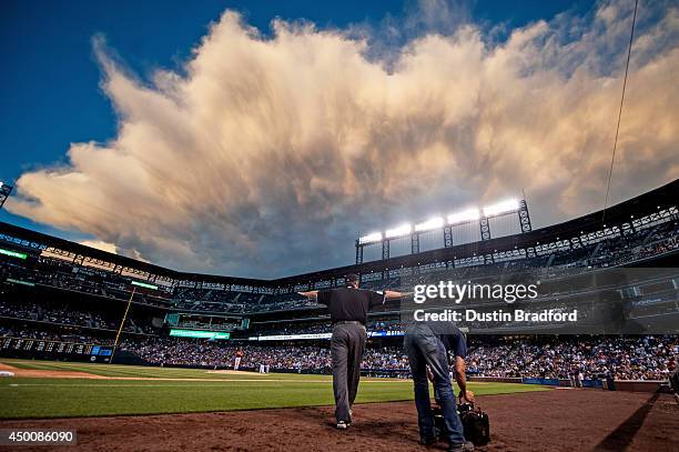 Umpire Jerry Layne upholds a safe call on a challenged play on a run scored by Troy Tulowitzki of the Colorado Rockies as clouds fill the sky over...