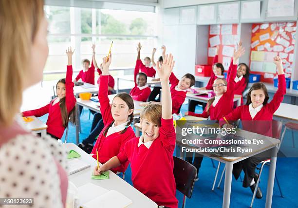 students with hands raised in classroom - teachers education uniform stock-fotos und bilder