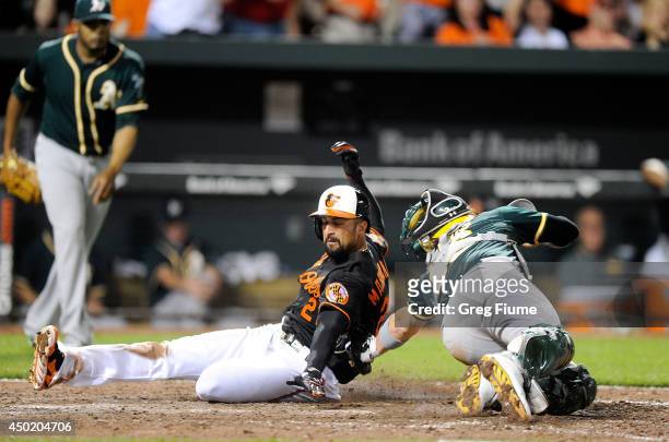 Nick Markakis of the Baltimore Orioles is tagged out at home plate in the tenth inning by Derek Norris of the Oakland Athletics at Oriole Park at...