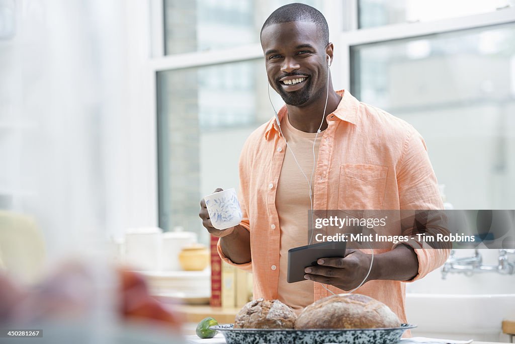 An office or apartment interior in New York City. A man in an orange shirt at the breakfast bar, having a cup of tea. 