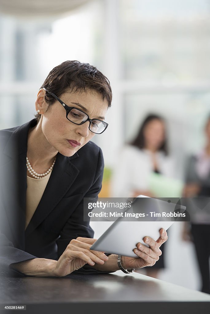 An office interior. A woman in a black jacket using a digital tablet.