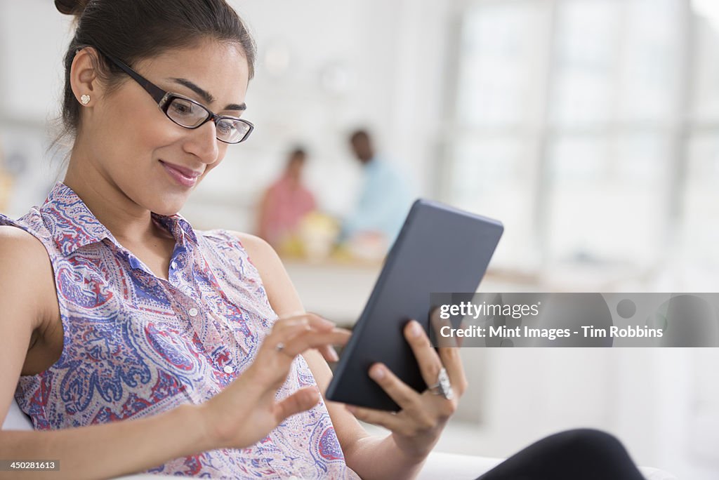 City office life in summer. A light and airy place of work. A young woman seated using a digital tablet.