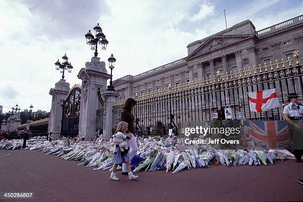 Buckingham Palace flowers laid for Diana, Princess of Wales - Woman and child walk past the floral tributes left outside the gates of Buckingham...