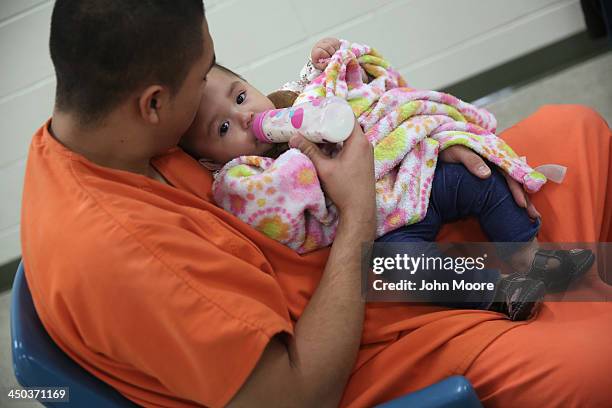 An immigrant detainee feeds his daughter during a family visitation visit at the Adelanto Detention Facility on November 15, 2013 in Adelanto,...