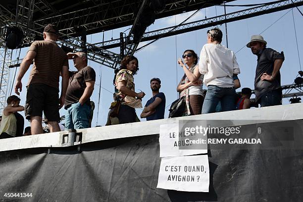 Entertainment industry workers and artists stand next to a banner hanging from a stage reading "The MEDEF is crossing a line - When is the Avignon...