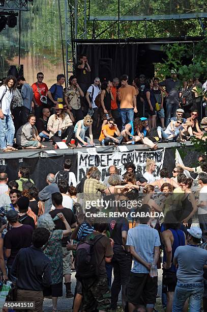 Entertainment industry workers and artists stand next to a banner hanging from a stage reading "MEDEF and Government - No to the agreement and the...