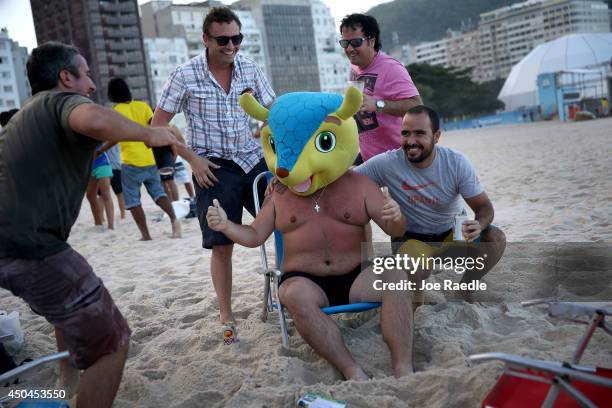 Argentinean soccer team fan, Cesar Ragazzini, from Argentina, wears the head of the FIFA mascot as he and his friends enjoy Copacabana beach while...