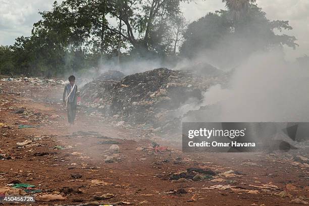 Young scavenger walks near a burning pile of trash in the Anlong Pi landfill on June 11, 2014 in Siem Reap, Cambodia. Dozens of children work every...